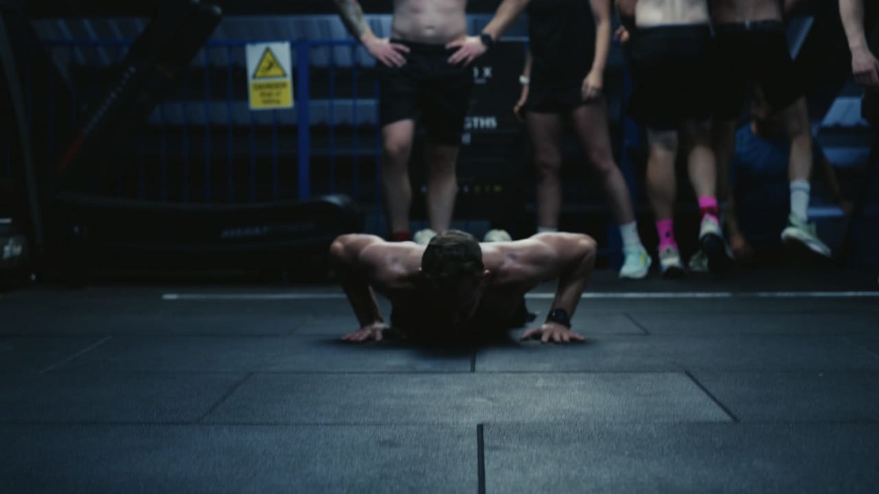 Athletes and spectators watching a burpee station during a gym fitness race