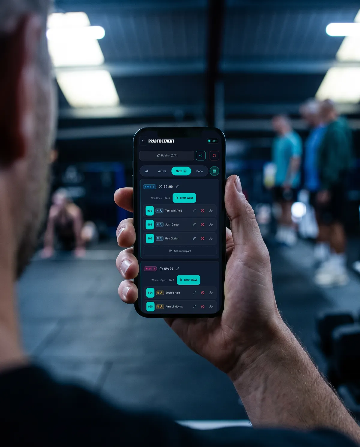 A judge's hand holding a phone showing the SimSplits live timing screen, with the gym's sim floor blurred behind